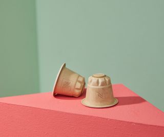 Cápsula de café de papel Nespresso lanzada sobre una superficie rosa